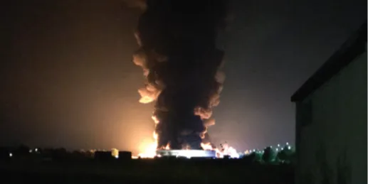 Incendie nocturne avec une épaisse colonne de fumée noire s'élevant dans le ciel sombre, illuminant légèrement l'horizon.